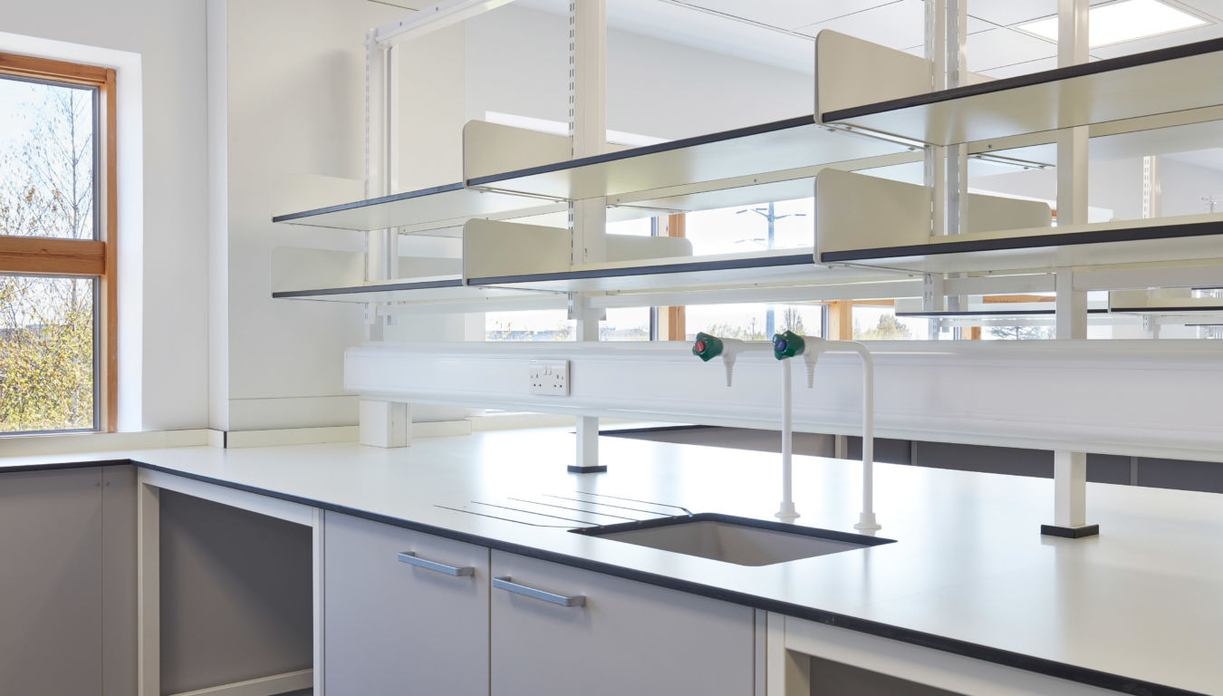 Bright and modern laboratory workspace featuring clean countertops, built-in cabinetry, glass shelving, and integrated water taps