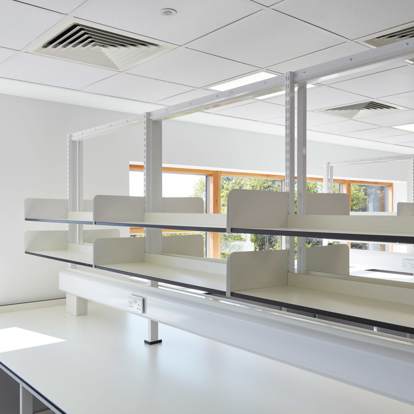 Bright laboratory space with white countertops, dual-sided shelving, and large windows allowing natural light into the room