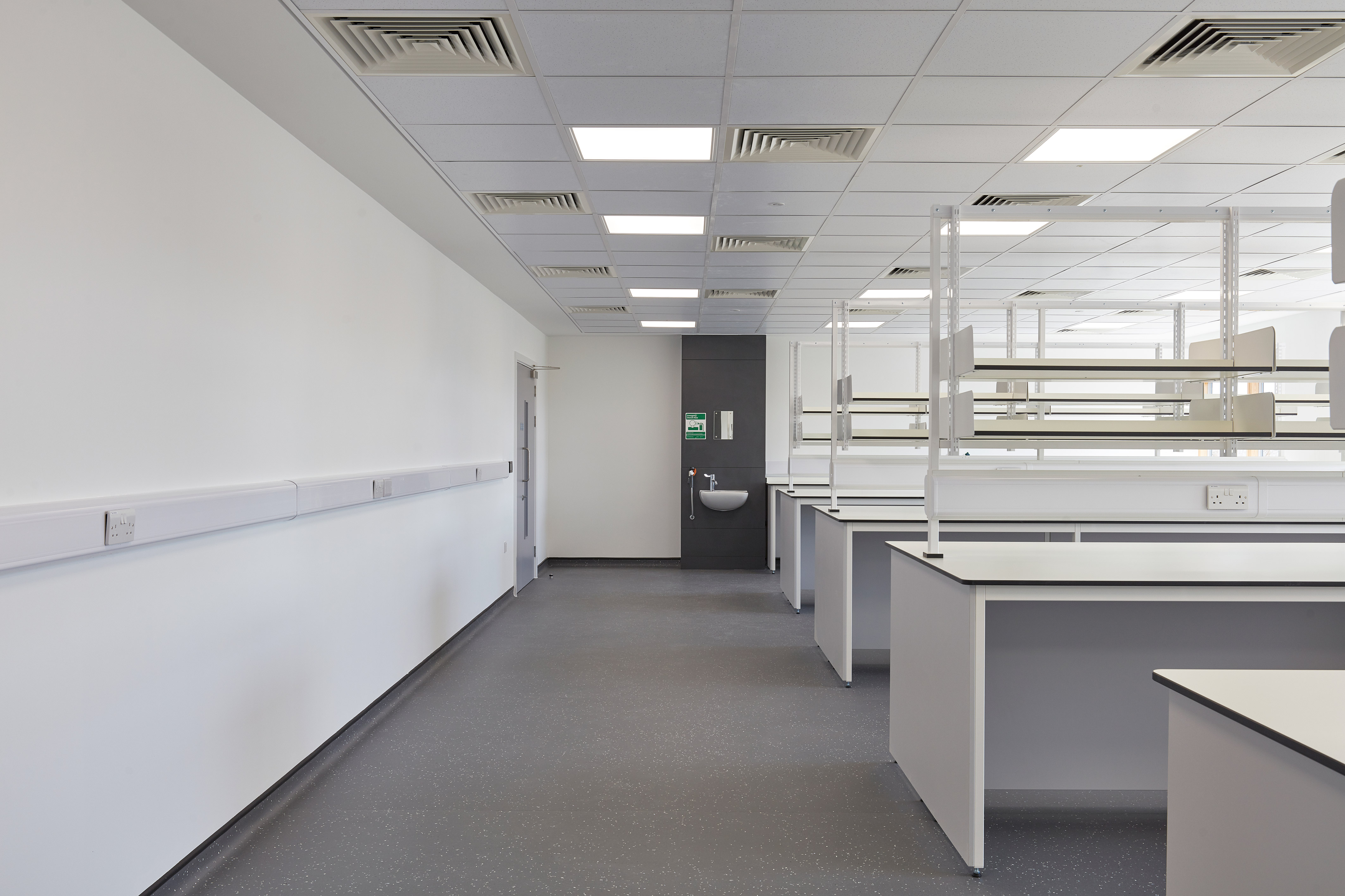 Modern laboratory interior with clean white workbenches, overhead shelving, and ceiling lighting.
