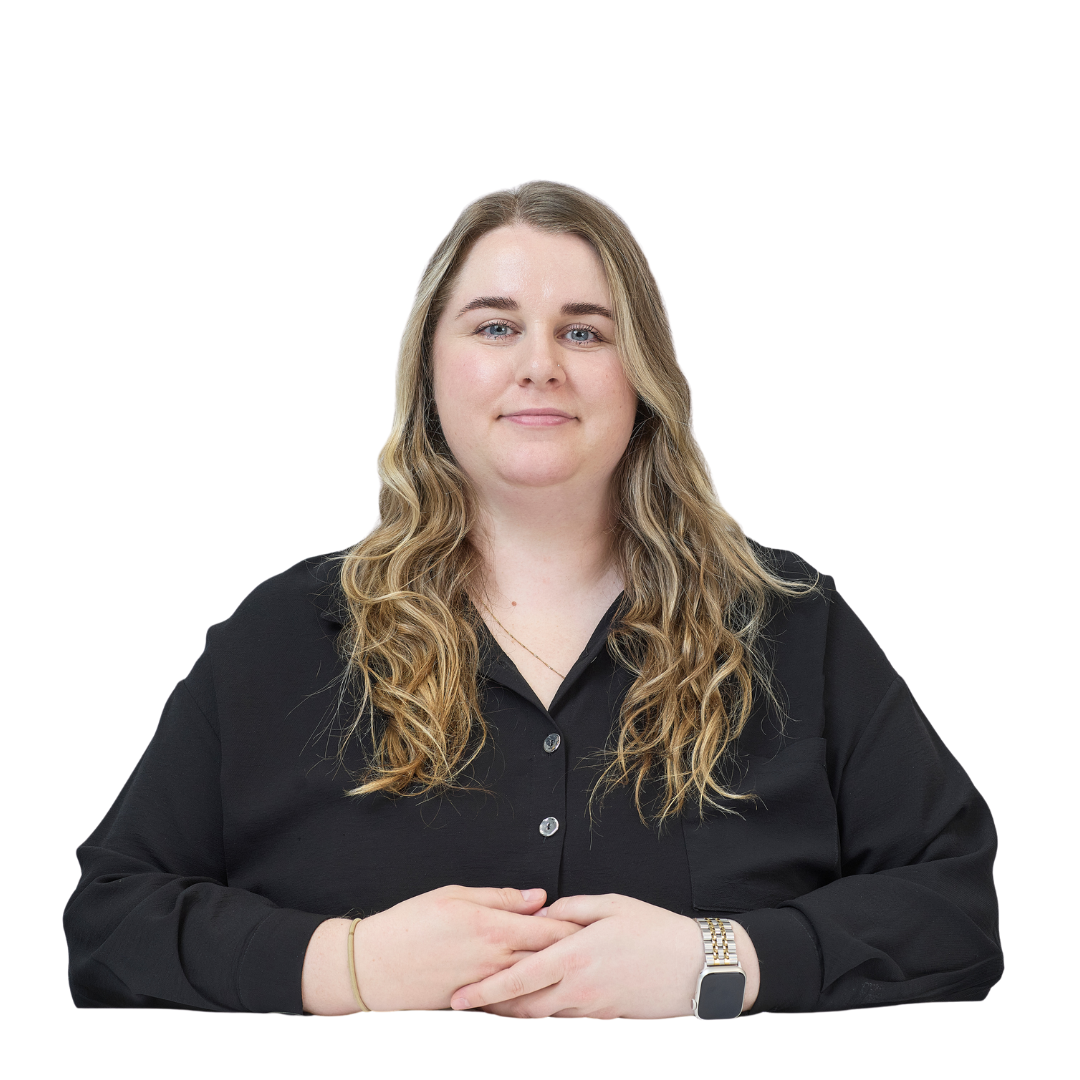 A person with long wavy hair and wearing a black shirt is seated, hands folded, against a plain white background.