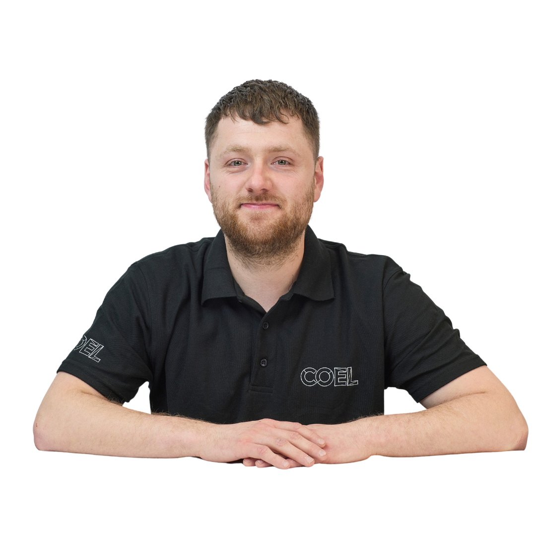 A man sits with his hands folded, wearing a black polo shirt featuring the logo “COEL,” on a plain white background.