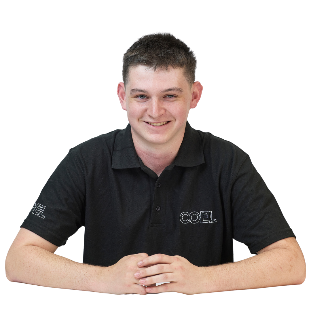 A person sits at a table, smiling, wearing a black polo shirt with "COEL" printed on it, against a plain white background.