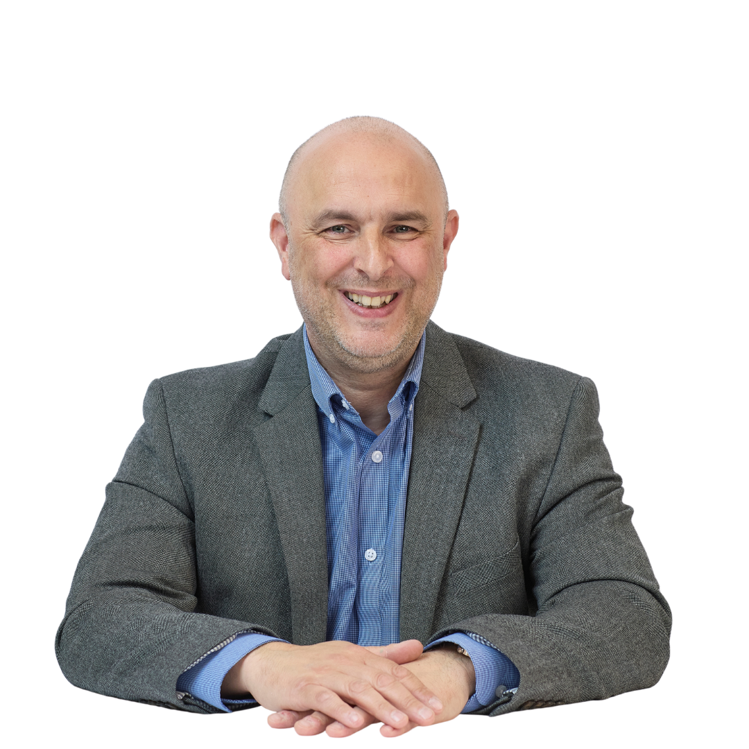 A man in a gray blazer and blue shirt sits smiling with hands folded, against a plain white background.