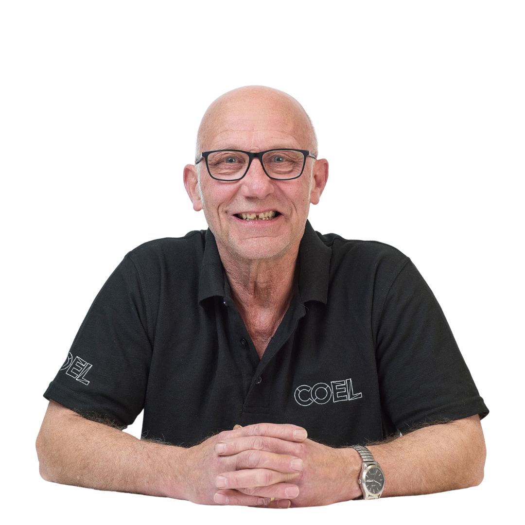 A person in a black shirt sits smiling, hands clasped, against a plain white background. The shirt has "COEL" embroidered on it.