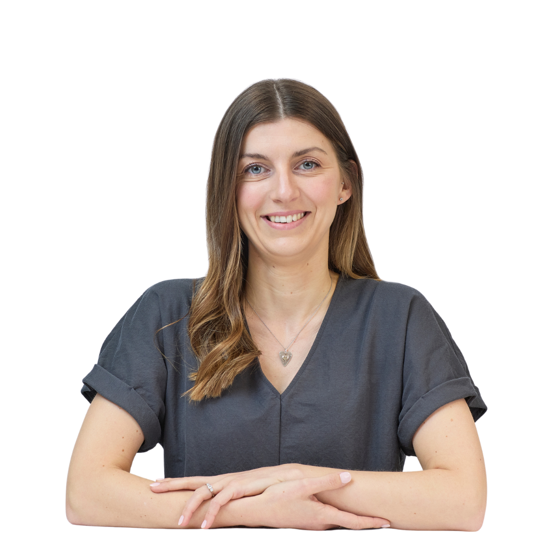 Smiling woman sitting with arms crossed, wearing a dark short-sleeved shirt and heart necklace, isolated on a plain white background.