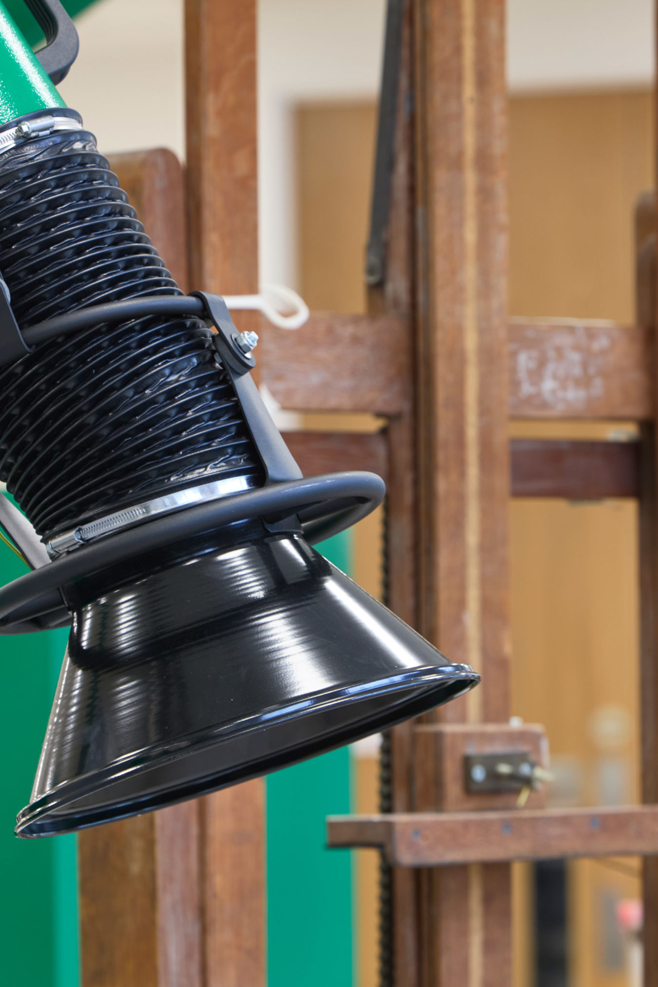 A green and black industrial exhaust hose extends over wooden frames in a workshop setting, likely used for ventilation or dust extraction.