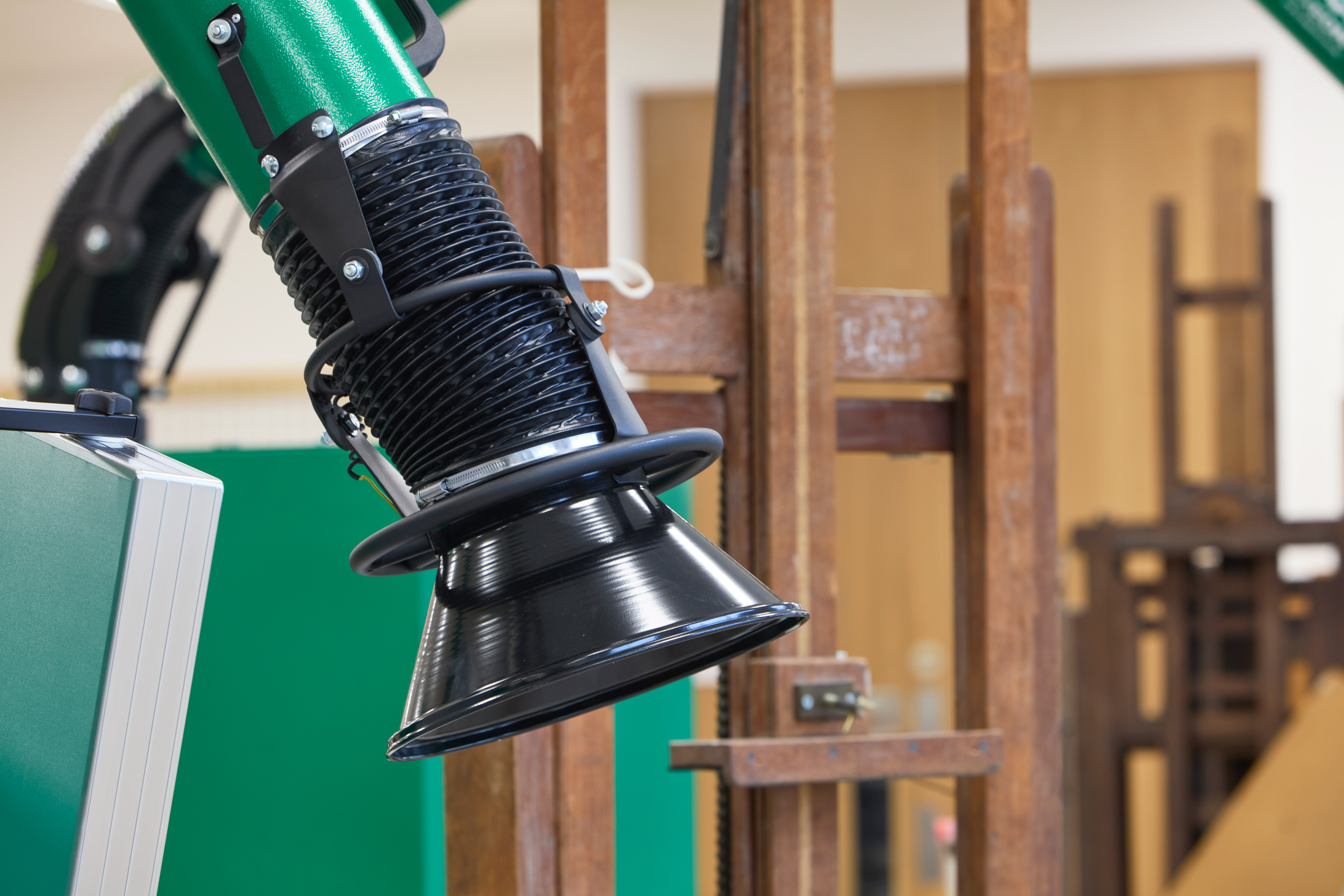 A green and black industrial exhaust hose extends over wooden frames in a workshop setting, likely used for ventilation or dust extraction.