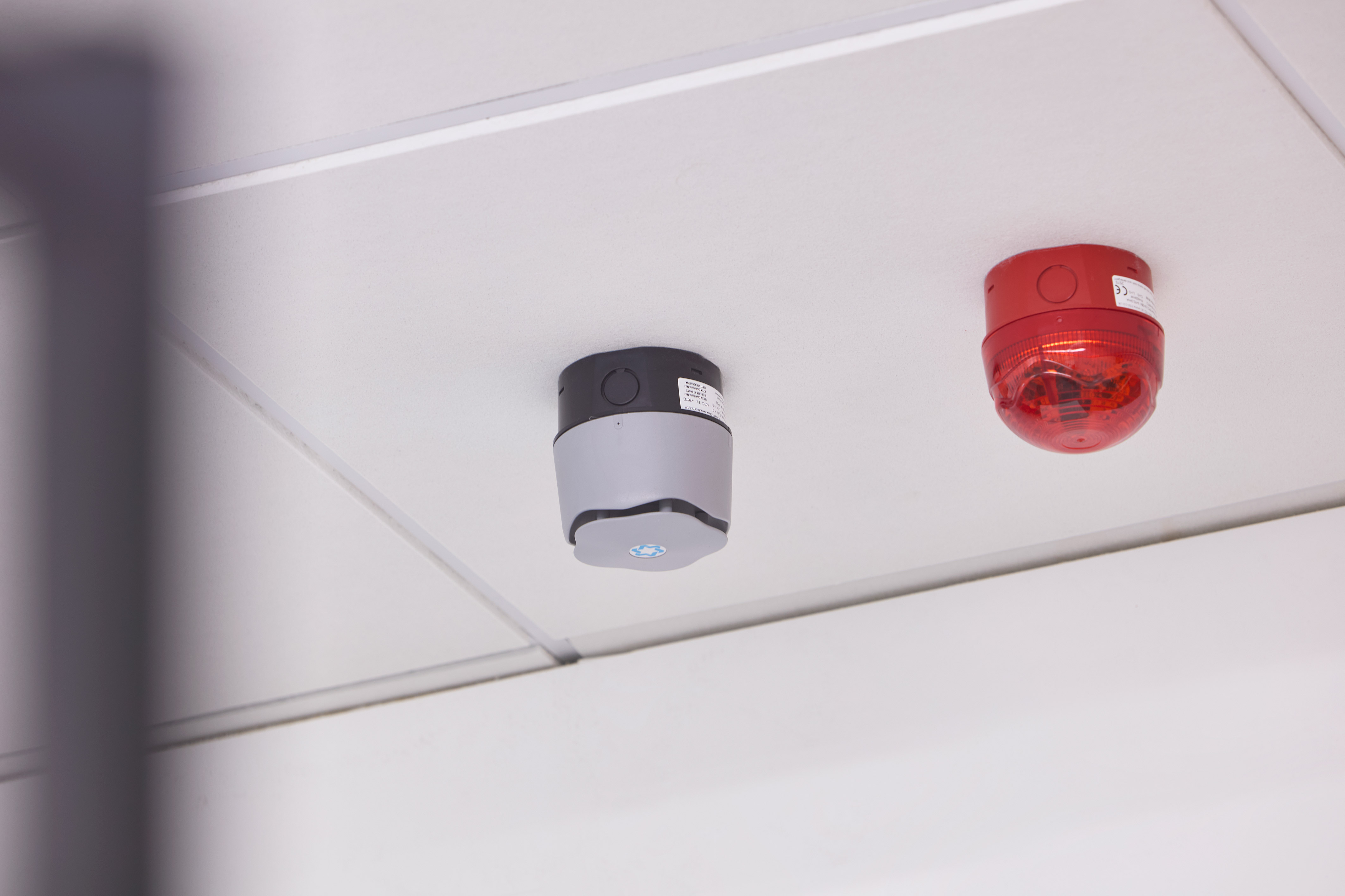 Smoke detector and red alarm device are installed on a white ceiling.