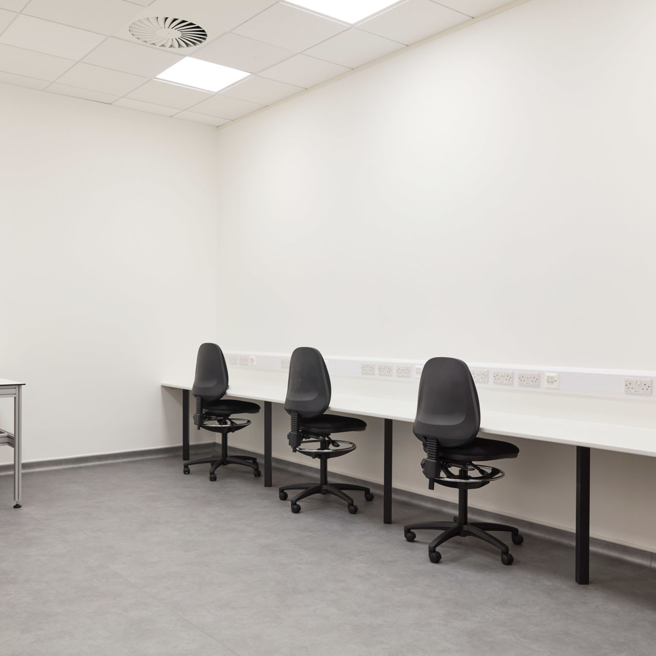 clean, sterile office with three black swivel chairs at a long white desk in a minimalist room. Neutral tones convey a calm, professional atmosphere