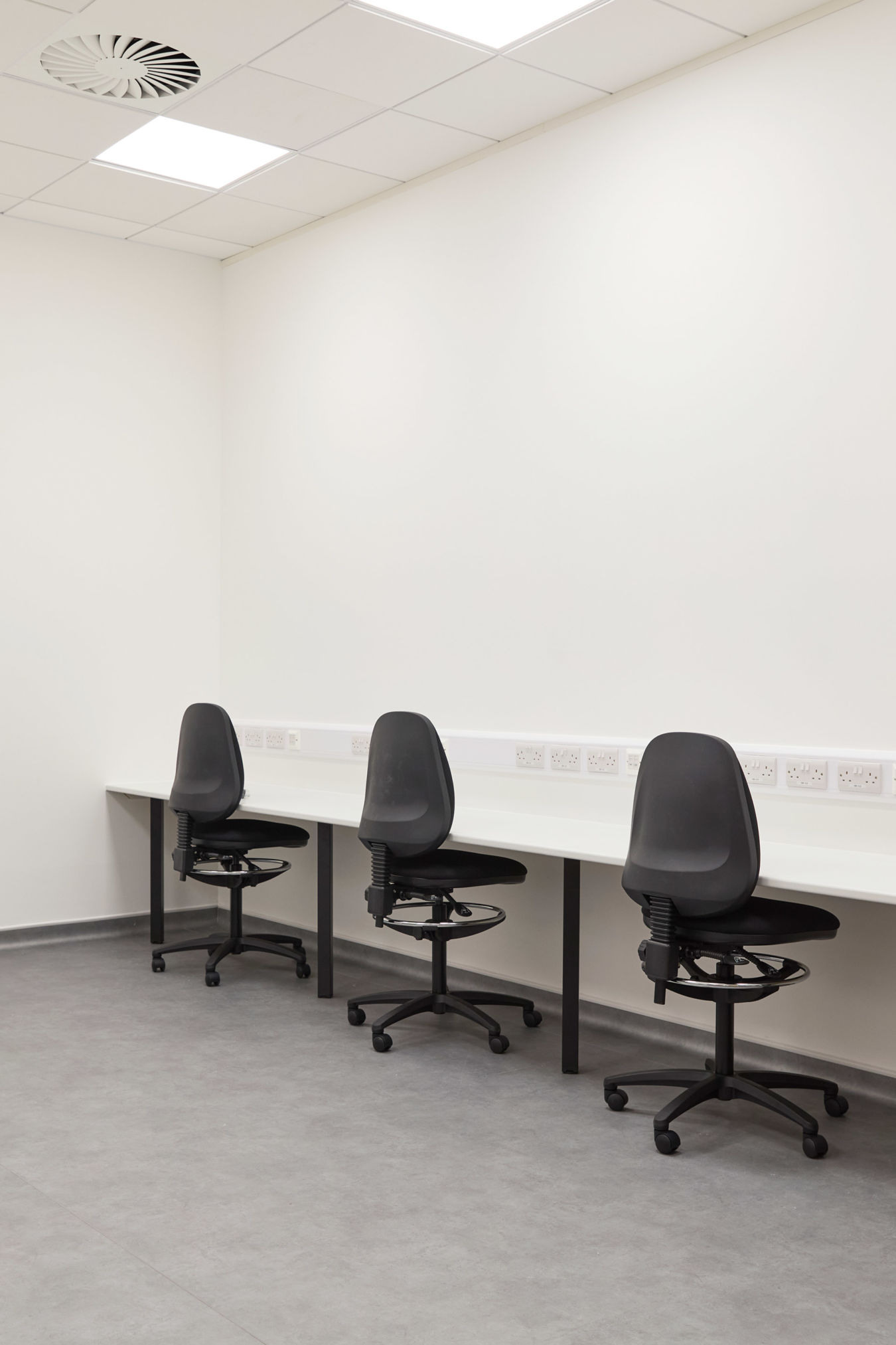 clean, sterile office with three black swivel chairs at a long white desk in a minimalist room. Neutral tones convey a calm, professional atmosphere