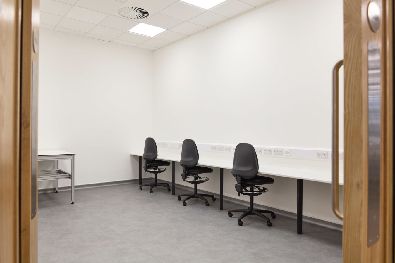clean, sterile office with three black swivel chairs at a long white desk in a minimalist room. Neutral tones convey a calm, professional atmosphere