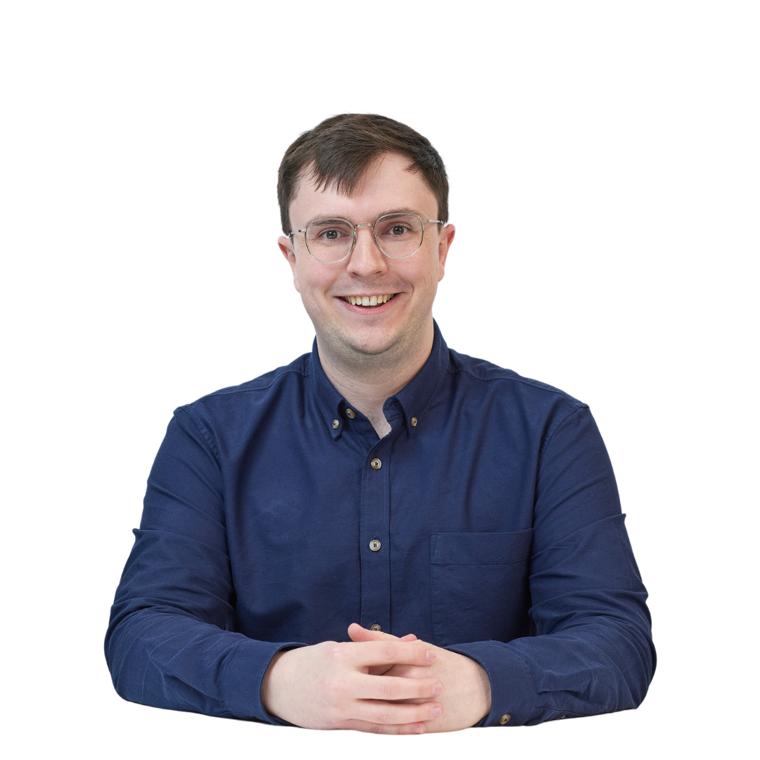 A person wearing glasses and a navy blue shirt sits at a table, smiling warmly at the camera, against a plain white background.