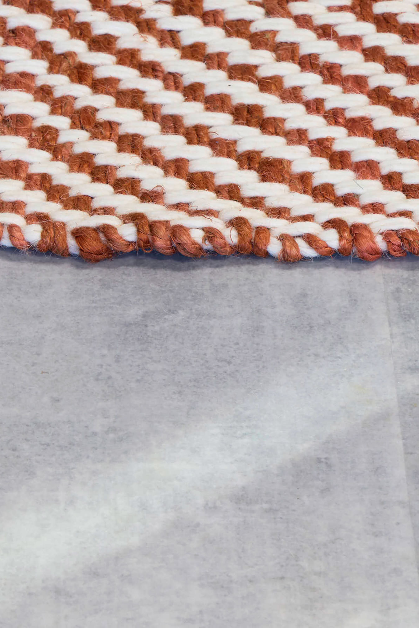 A close-up of a woven rug displaying a brown and white chevron pattern, resting on a smooth, light gray surface.