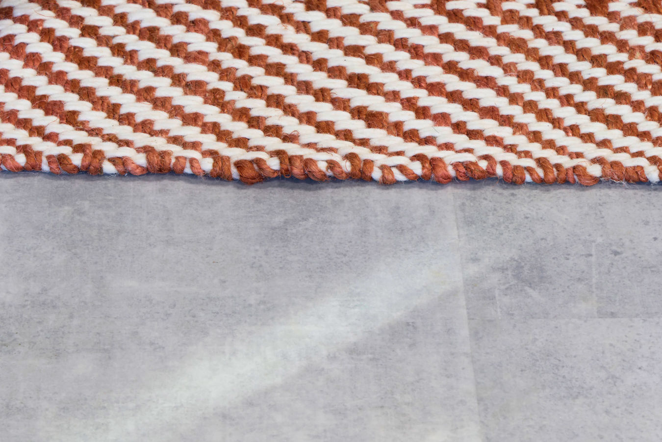 A close-up of a woven rug displaying a brown and white chevron pattern, resting on a smooth, light gray surface.