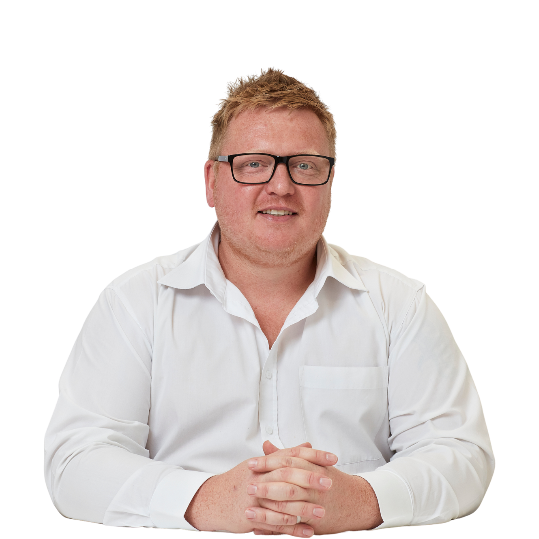 A person wearing glasses and a white shirt sits with hands clasped on a white surface against a plain white background.