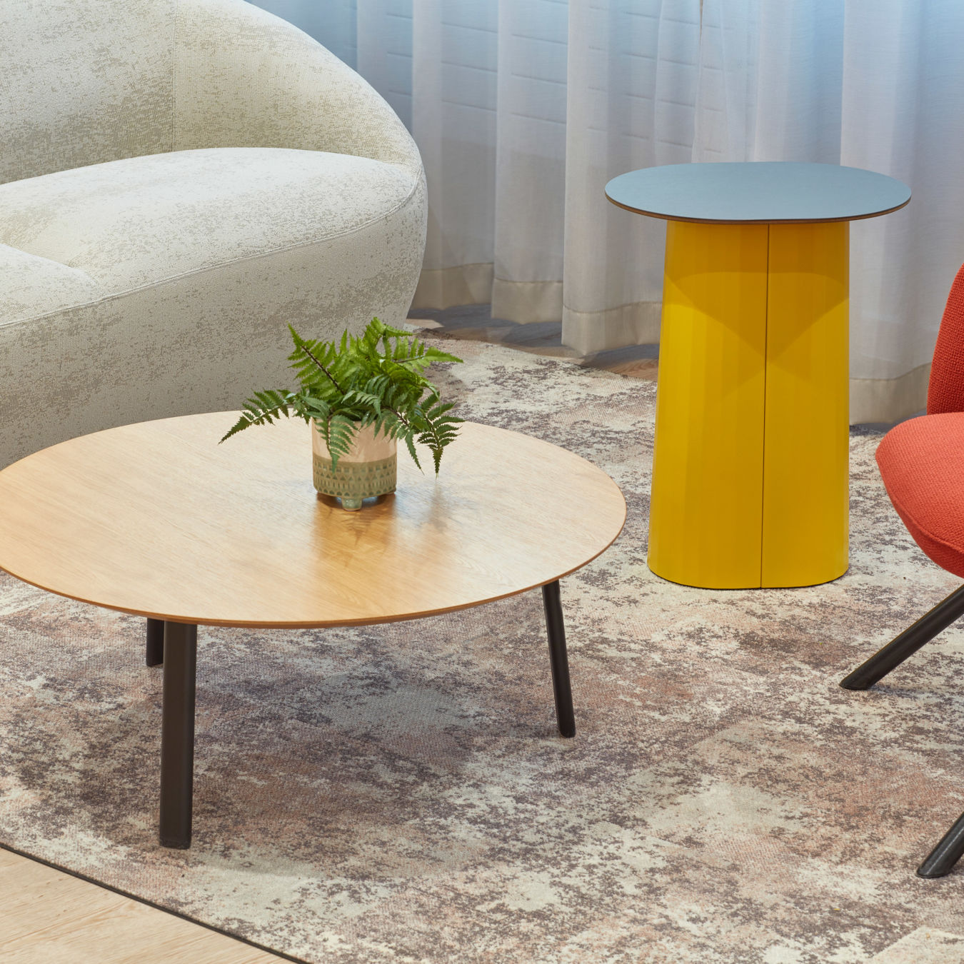 Close-up of a modern lounge area featuring a round wooden coffee table with a potted plant, a yellow side table, and contemporary seating.