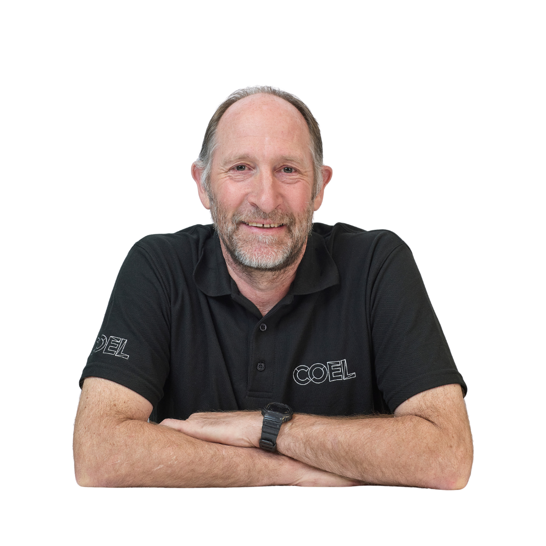 A person wearing a black polo shirt with "COEL" white text smiles while resting arms on a surface; background is plain white.