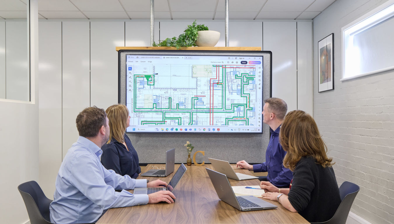 brightly lit, modern office with rows of empty desks, ergonomic chairs, and large windows