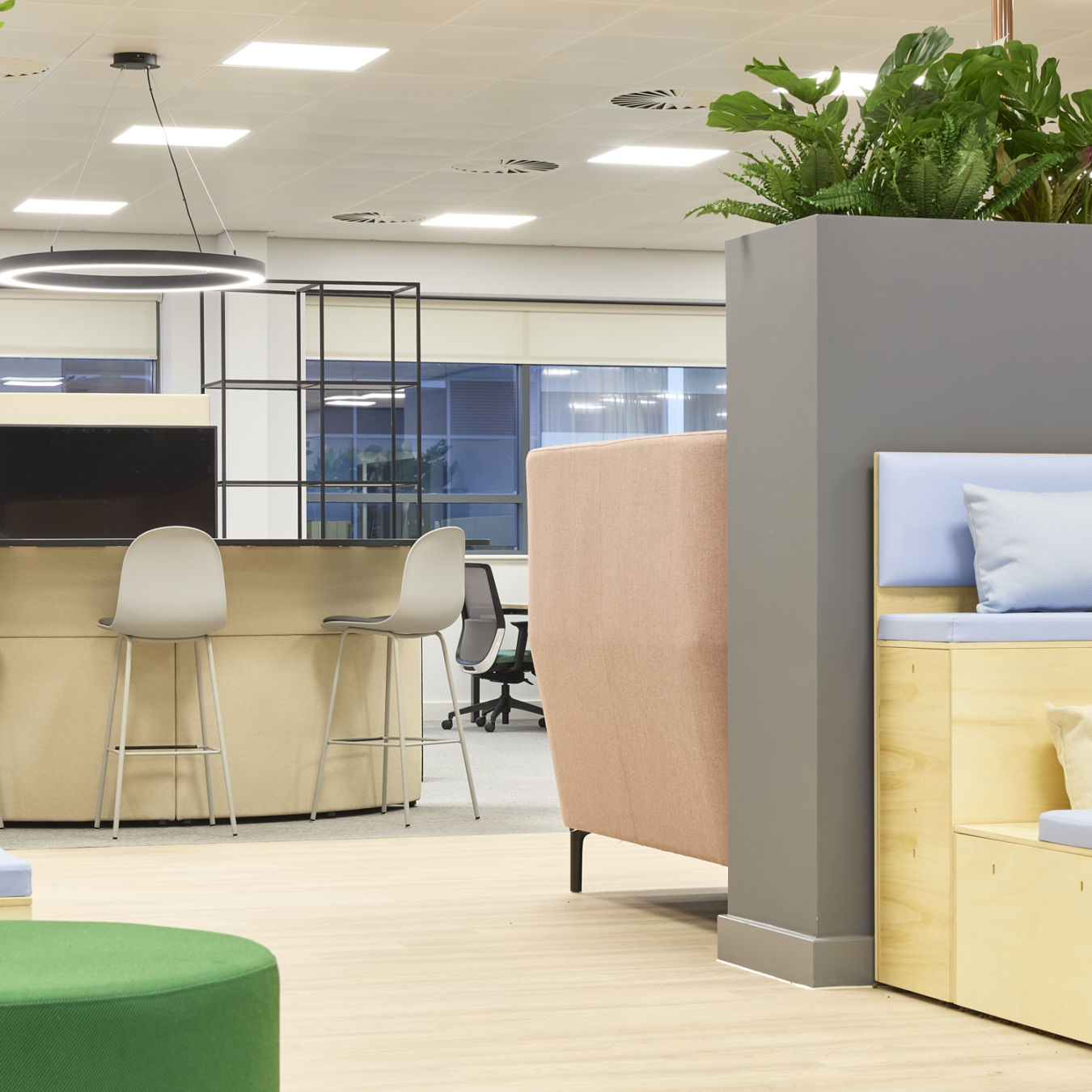 Open-plan office with mixed seating, high counter stools, soft furnishings, indoor plants, and modern lighting