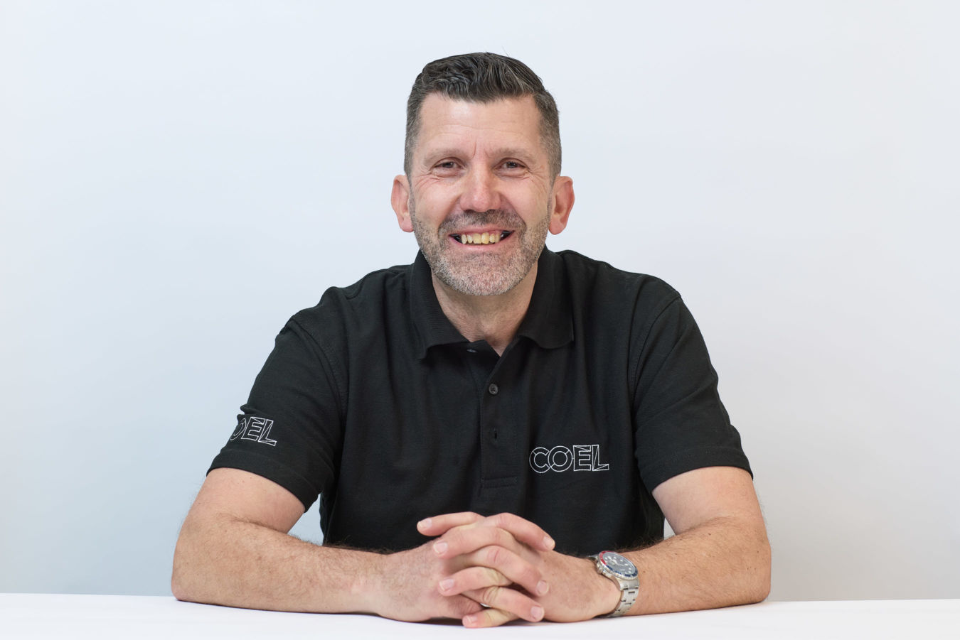 Man smiling with arms crossed, wearing a black COEL-branded polo shirt against a plain white background.
