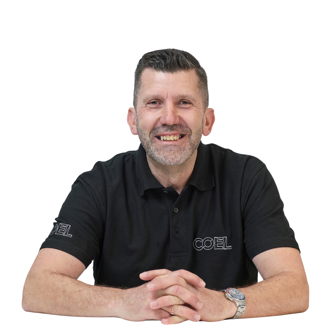 Smiling man in a black polo shirt with "COEL" logo sits at a table against a white background, hands clasped with a visible wristwatch.