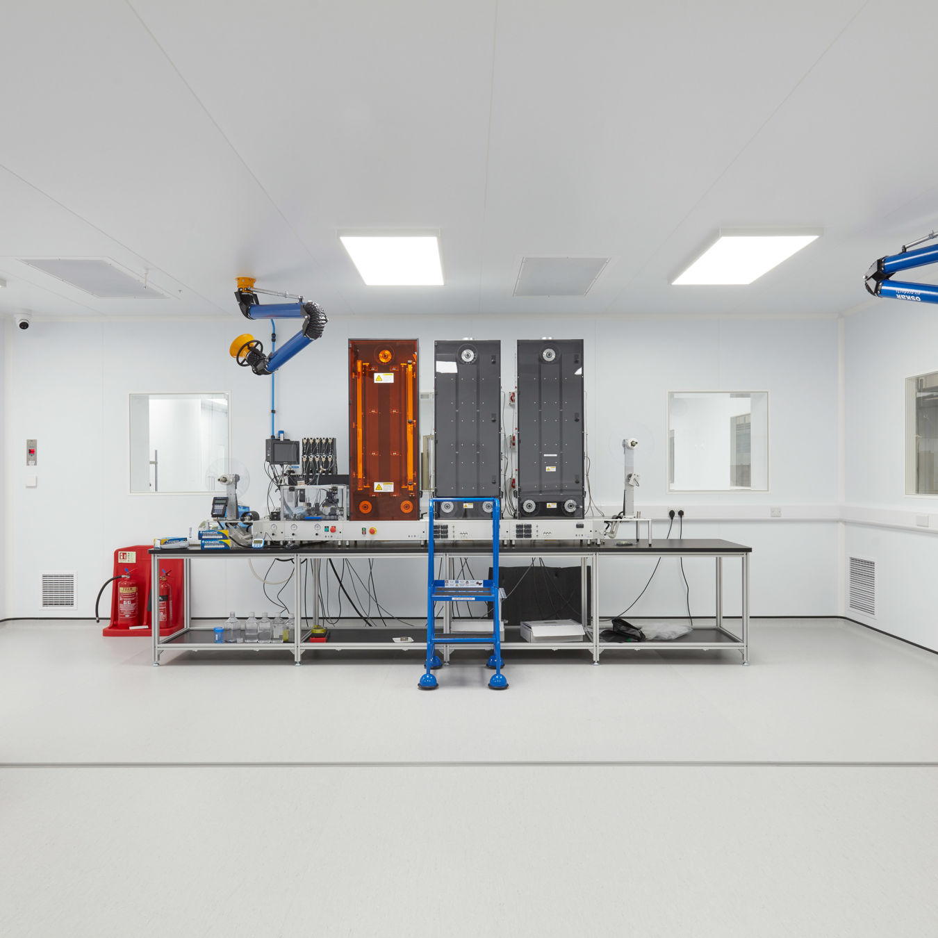 sterile, modern lab with clean white walls features industrial equipment, a blue ladder, and ceiling-mounted machinery, creating a clinical, precise atmosphere