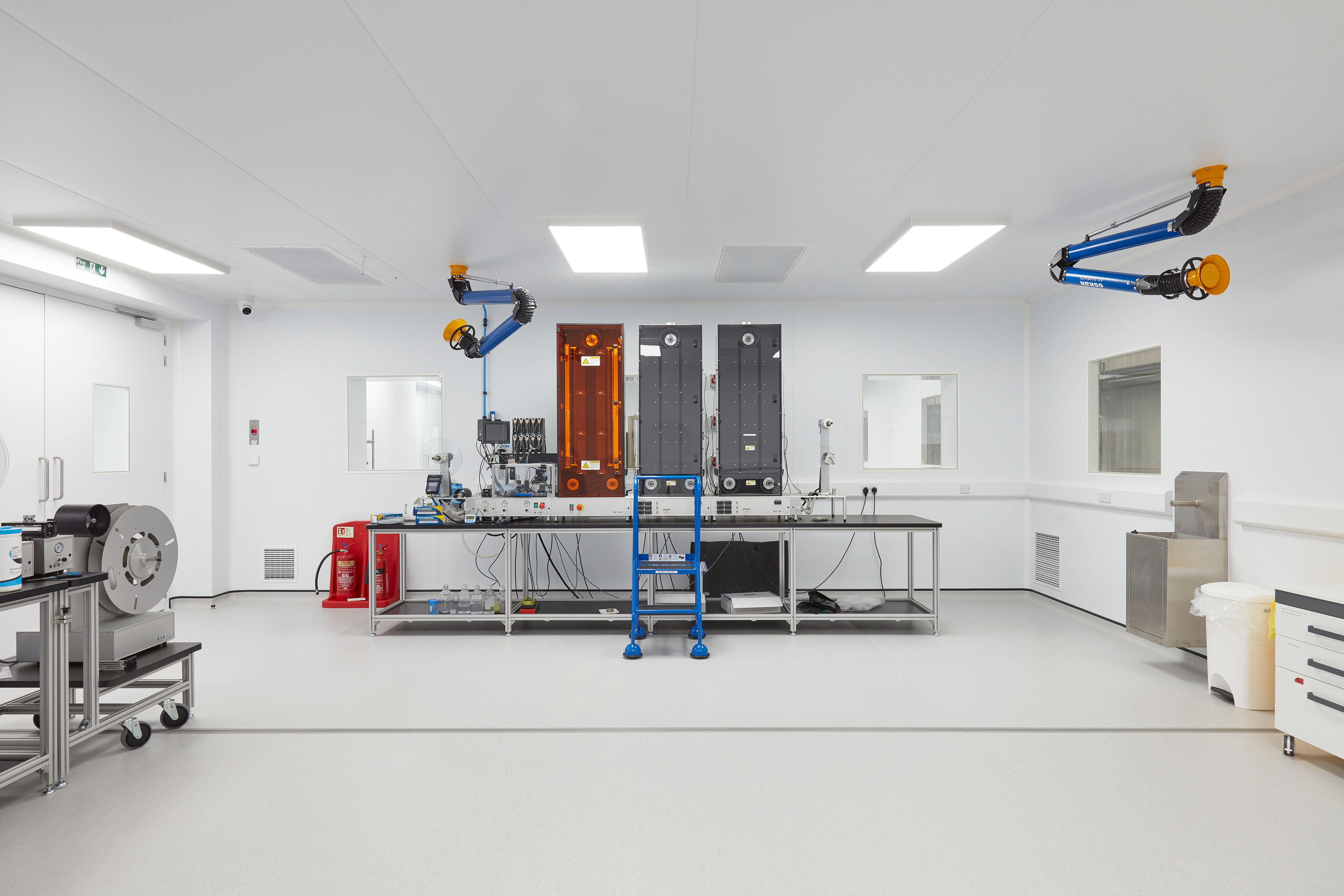 sterile, modern lab with clean white walls features industrial equipment, a blue ladder, and ceiling-mounted machinery, creating a clinical, precise atmosphere