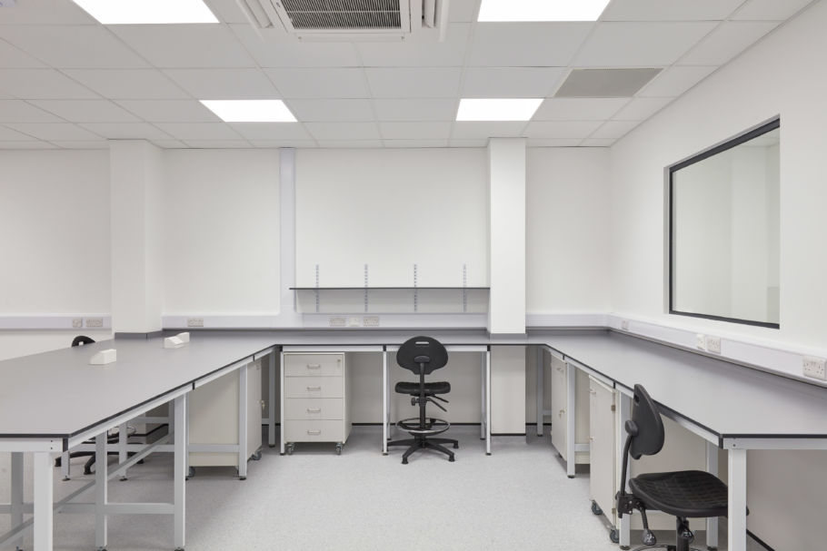 Clean and organized laboratory with U-shaped workbenches, rolling lab chairs, under-counter drawers, and a bright ceiling light grid.