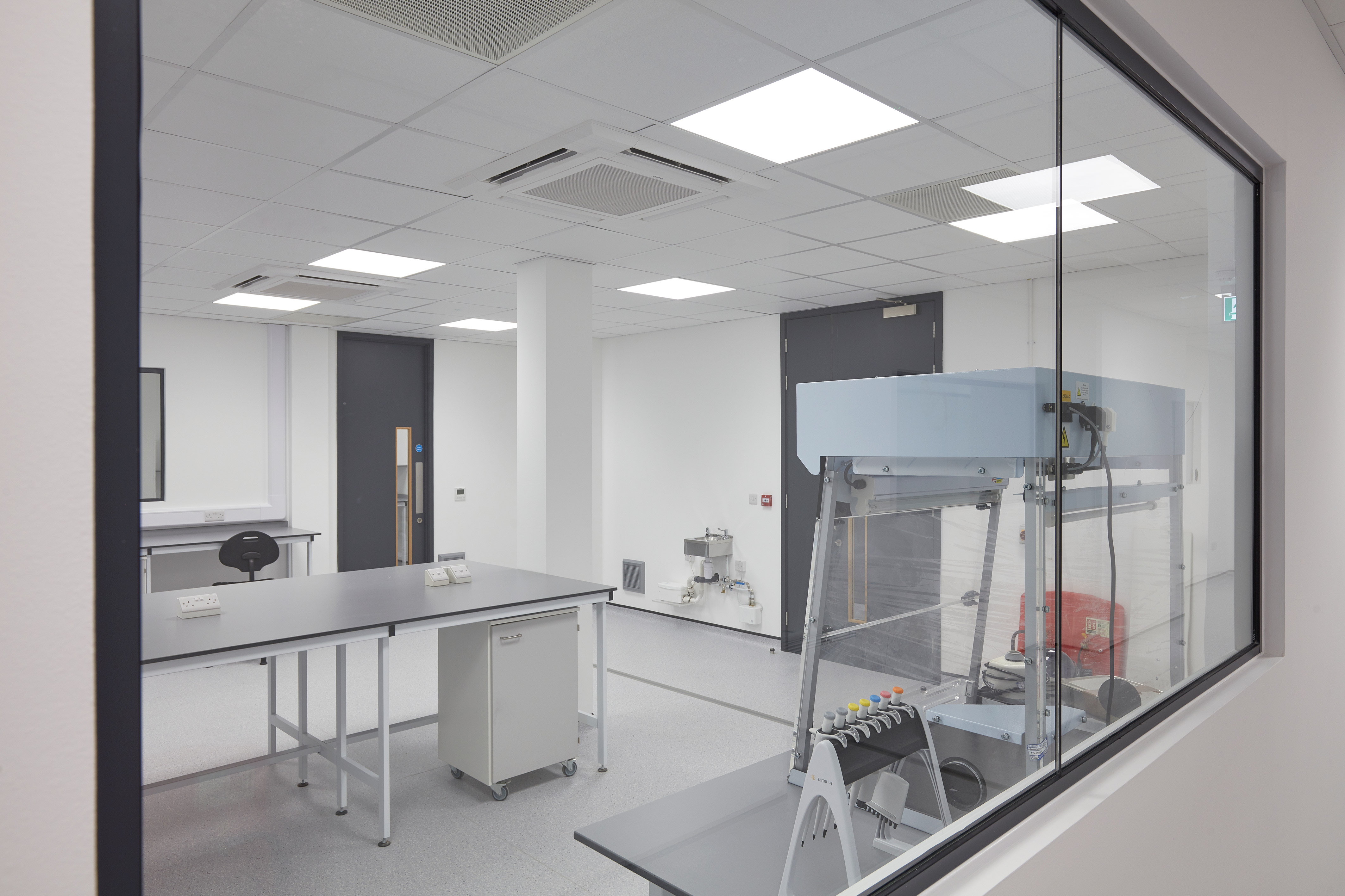 View through glass partition into a laboratory with workstations and specialised equipment, part of a COEL lab fit-out for Sense Bio.