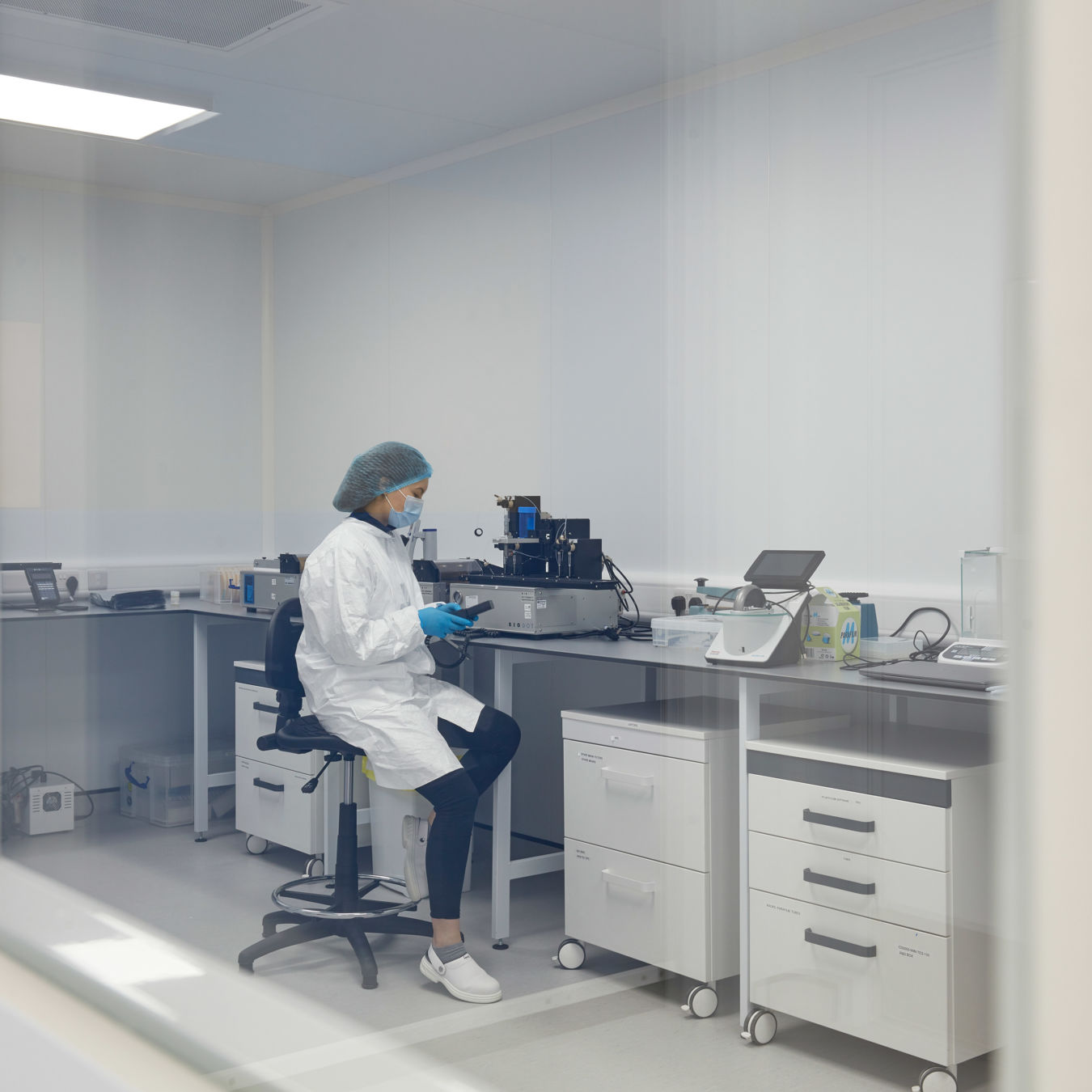 scientist in a lab coat and gloves works alone at a lab bench, surrounded by equipment and storage. The scene is calm and methodical