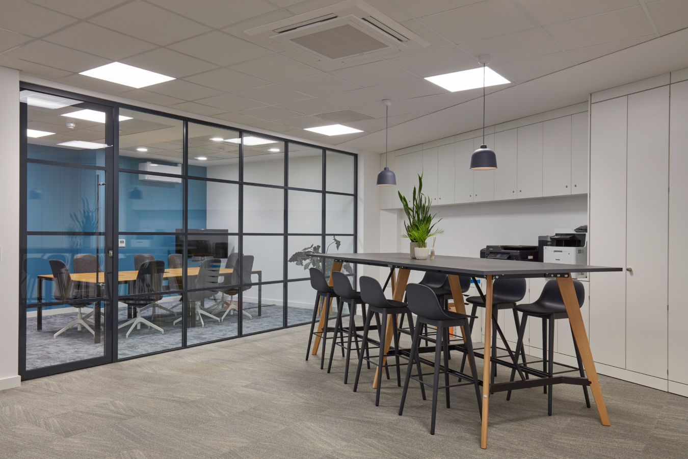 Modern breakout area with high table seating and glass-walled meeting rooms, part of a COEL office fit-out for Sense Bio.