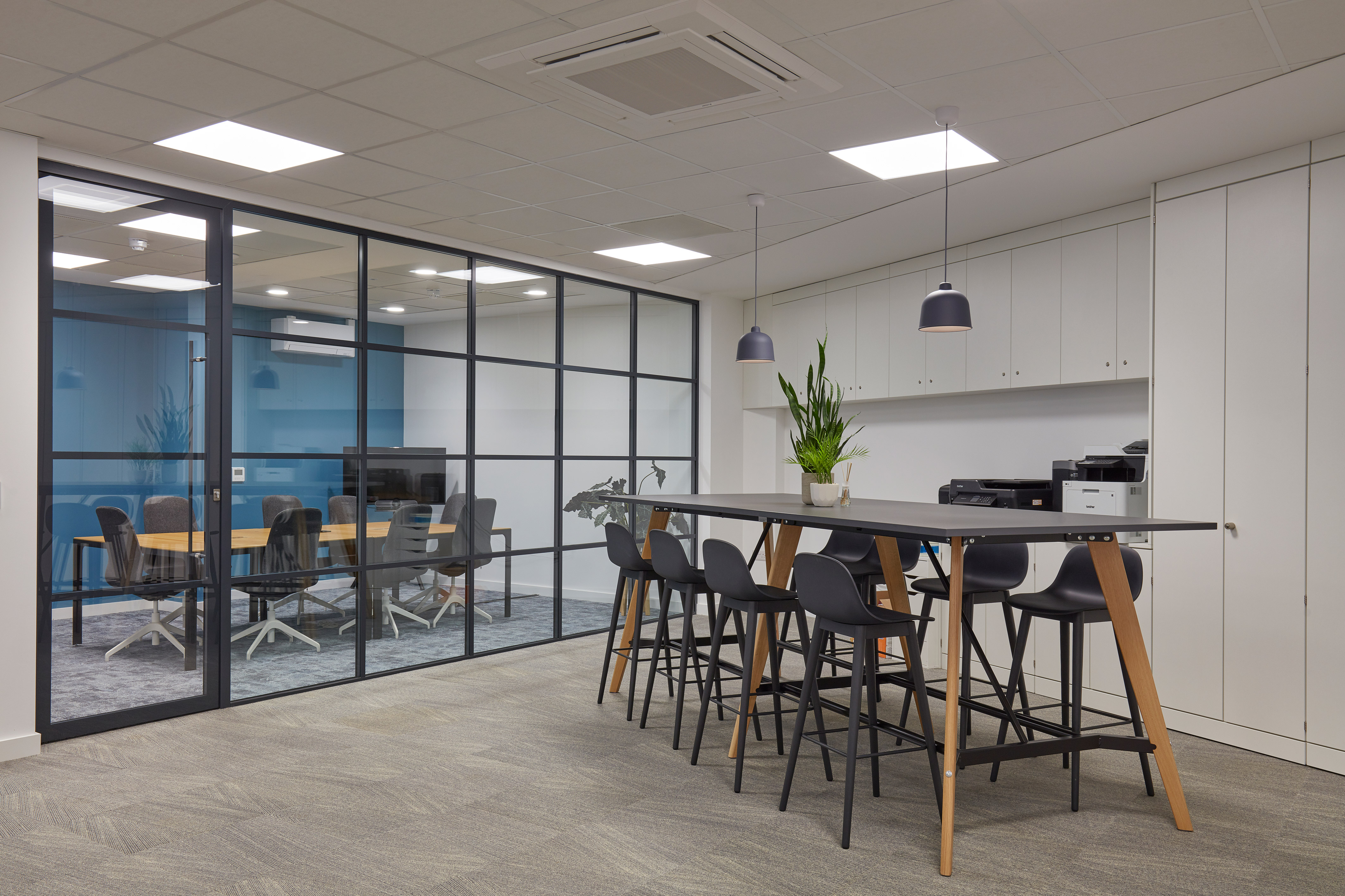 Modern breakout area with high table seating and glass-walled meeting rooms, part of a COEL office fit-out for Sense Bio.