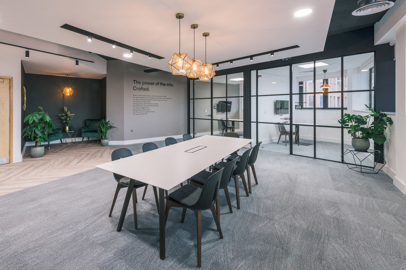Modern office with a sleek conference room featuring a long white table and black chairs. Glass walls reveal an adjacent workspace. Elegant pendant lights and greenery add warmth.
