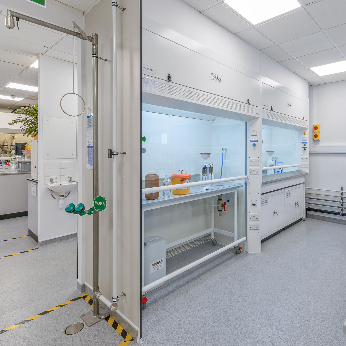 Well-equipped laboratory with a fume hood workstation, emergency shower and eyewash station, bright overhead lighting, and clean, organized surfaces