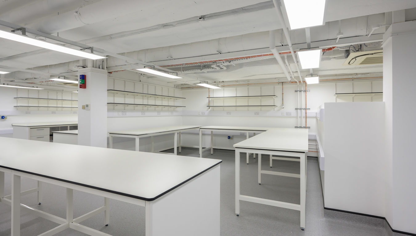 Bright, white laboratory space with multiple workbenches, open shelving, and exposed ceiling fixtures.