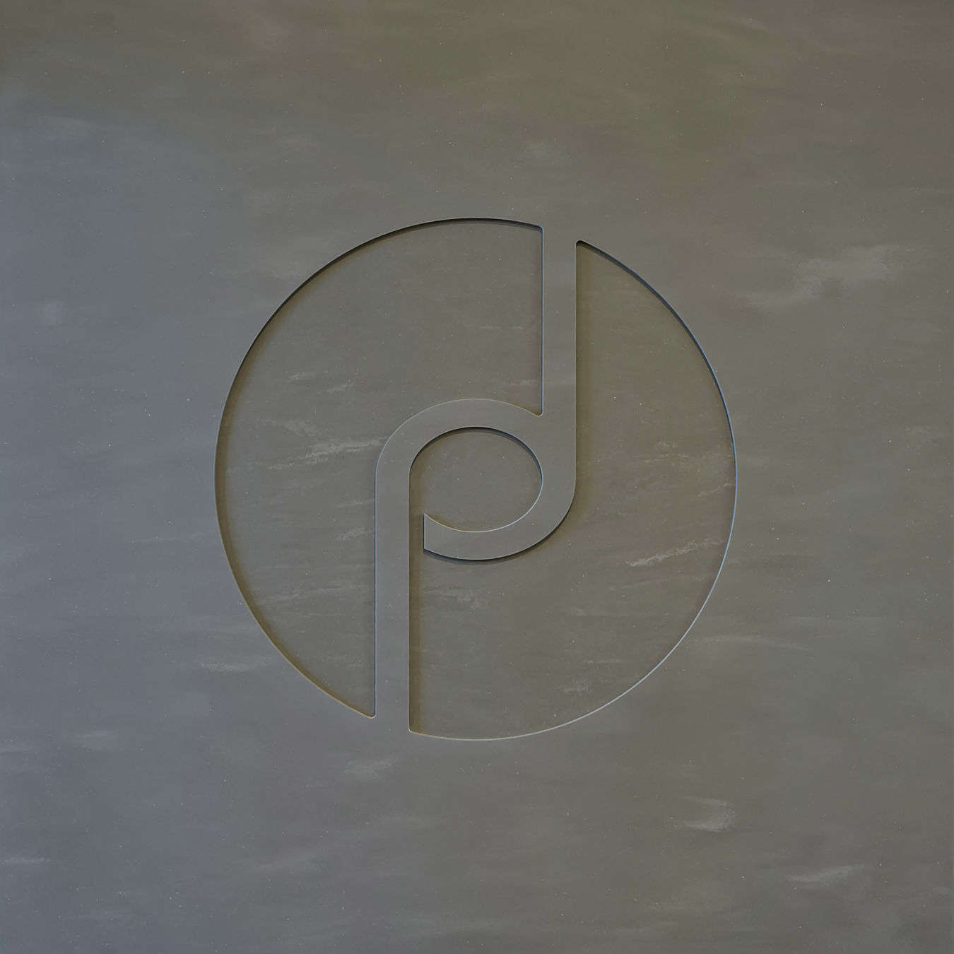 Abstract circular logo design with a cut-out pattern, featuring a curved line and circle intersecting, set against a textured gray background.