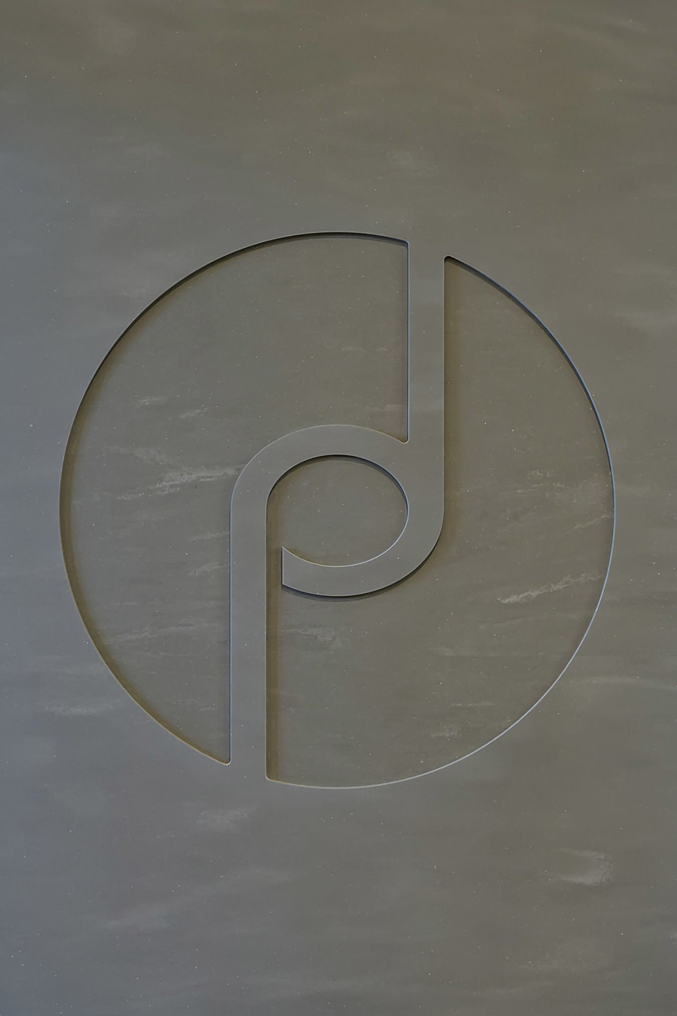Abstract circular logo design with a cut-out pattern, featuring a curved line and circle intersecting, set against a textured gray background.