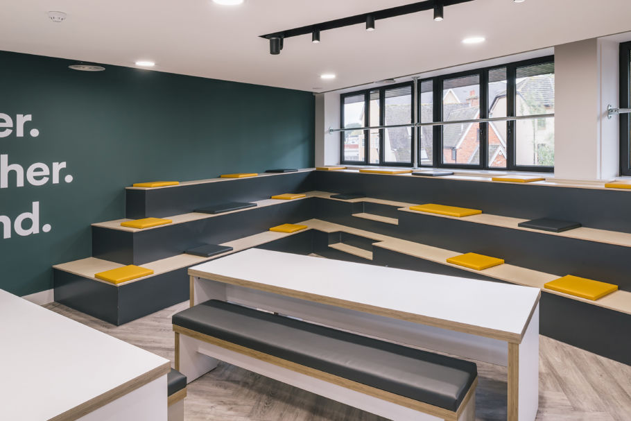 Modern room with tiered seating featuring black and yellow cushions. Bright windows and green walls create an open, inviting atmosphere