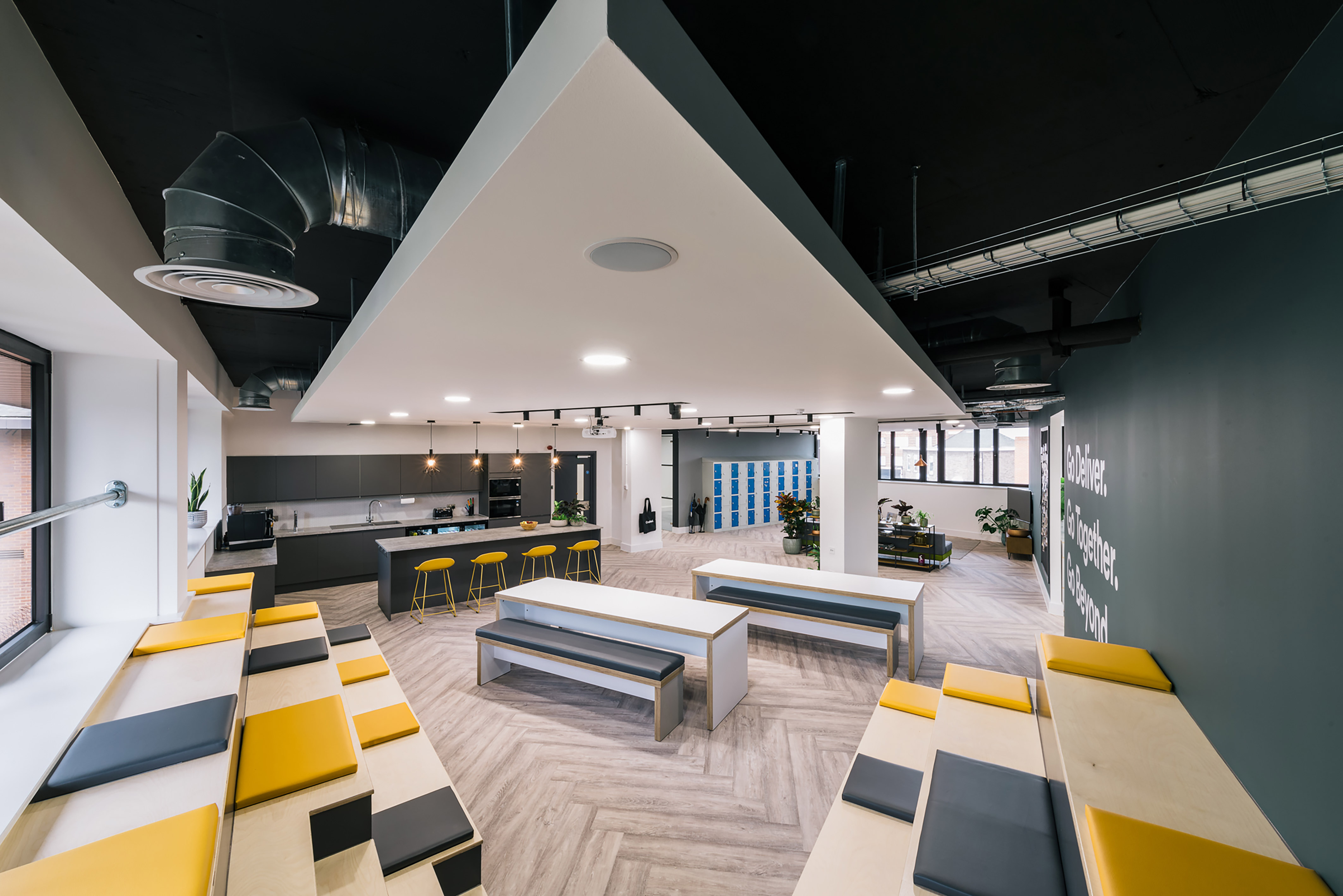 Modern office space with yellow and gray seating, a central kitchen island with bar stools, and open, airy design. Bright lighting creates a welcoming feel