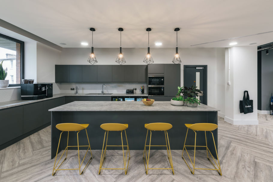 Modern kitchen with gray cabinets, marble countertop island, and four yellow barstools. Overhead pendant lights create a warm, inviting ambiance