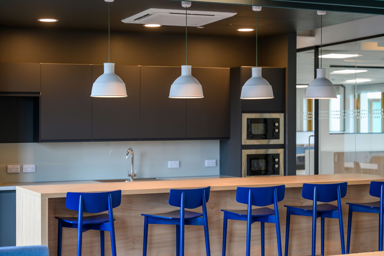 modern corporate kitchen with dark cabinetry, light wooden countertops, and blue bar stools under pendant lights
