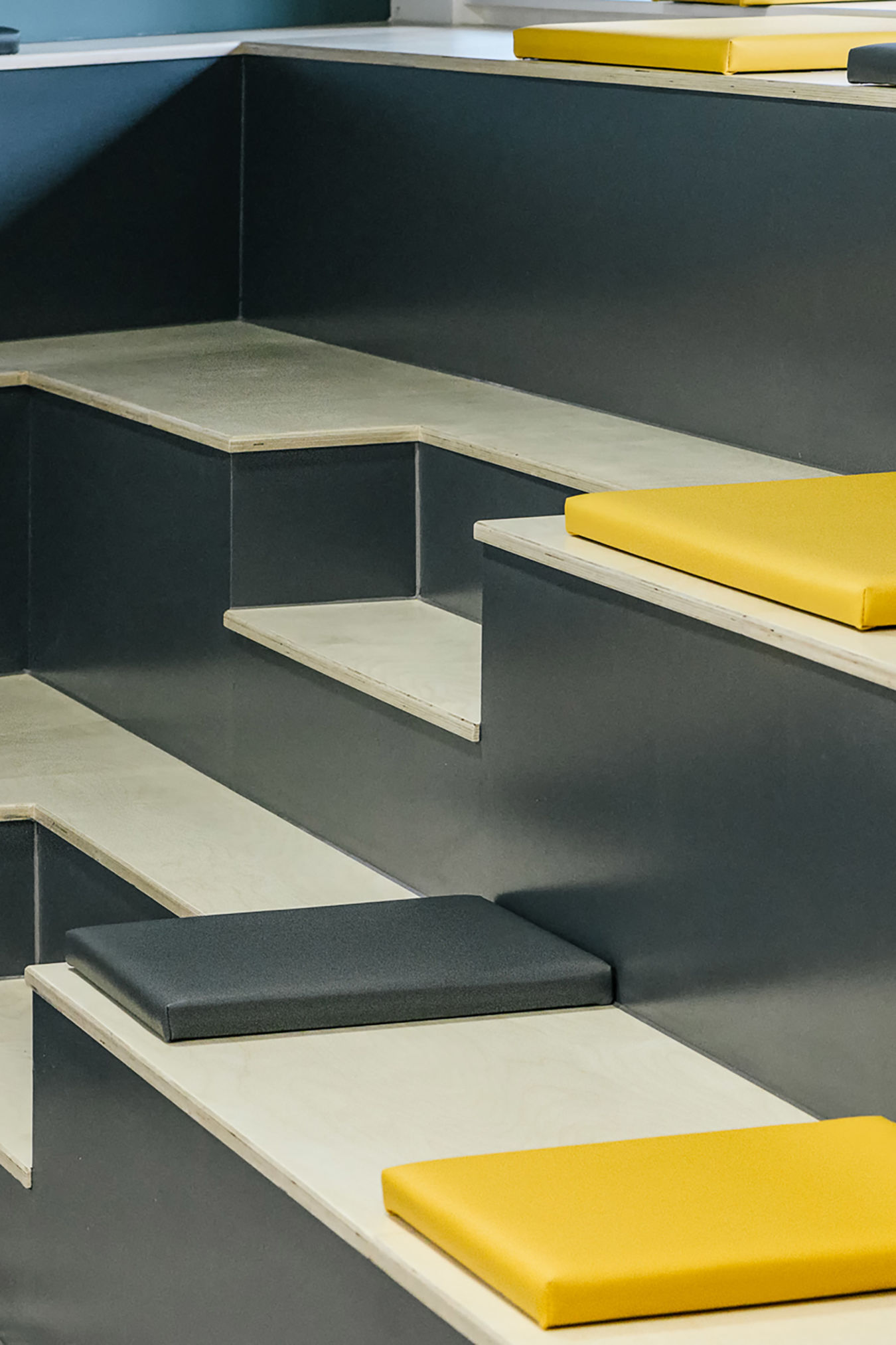 Modern stepped seating area with wooden benches and yellow and gray square cushions. The design is minimalistic, evoking a calm, organized atmosphere