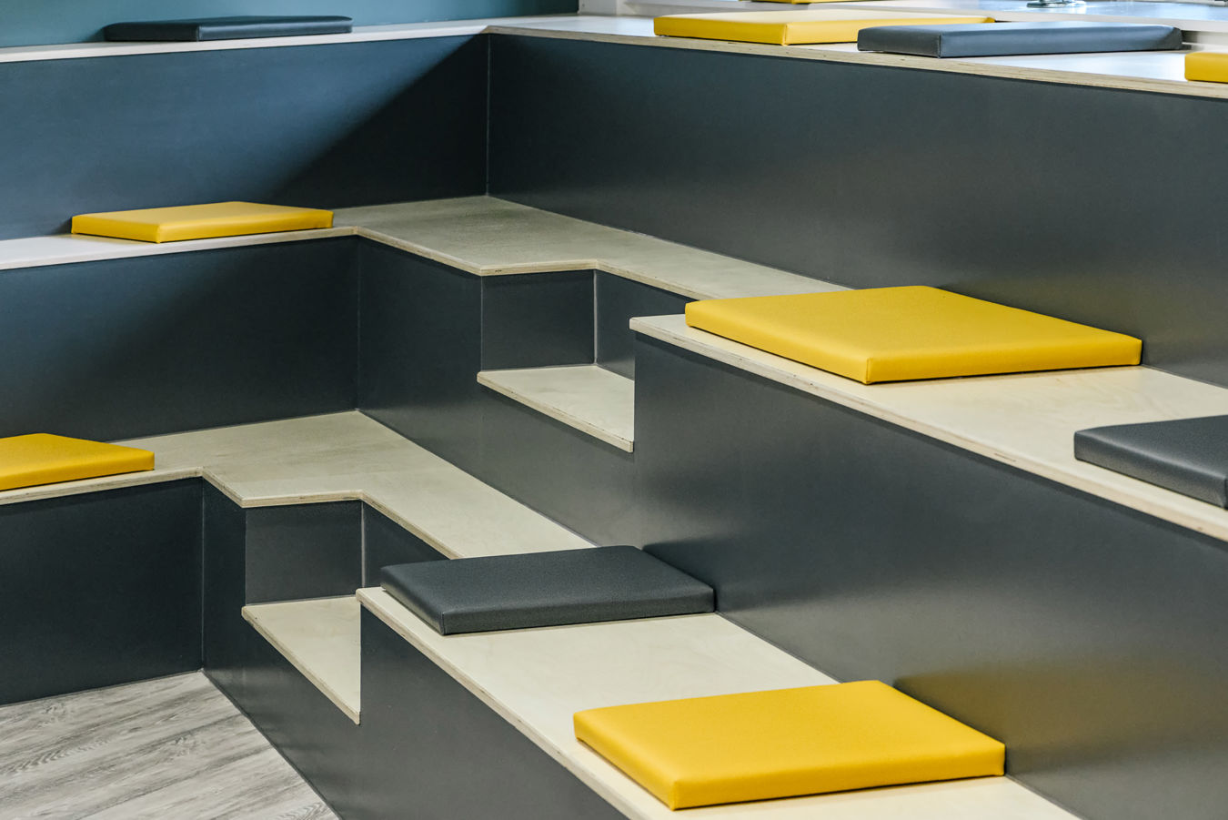 Modern stepped seating area with wooden benches and yellow and gray square cushions. The design is minimalistic, evoking a calm, organized atmosphere