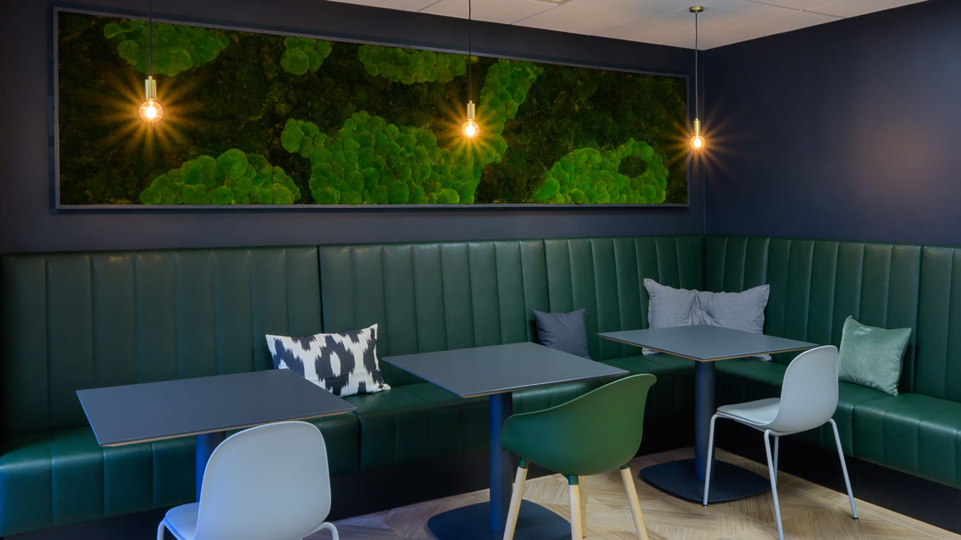 dark green leather booth seating and two sleek tables. Warm pendant lights hang above, casting a cozy glow. A vibrant green textured artwork adorns the deep blue wall, enhancing the calming atmosphere