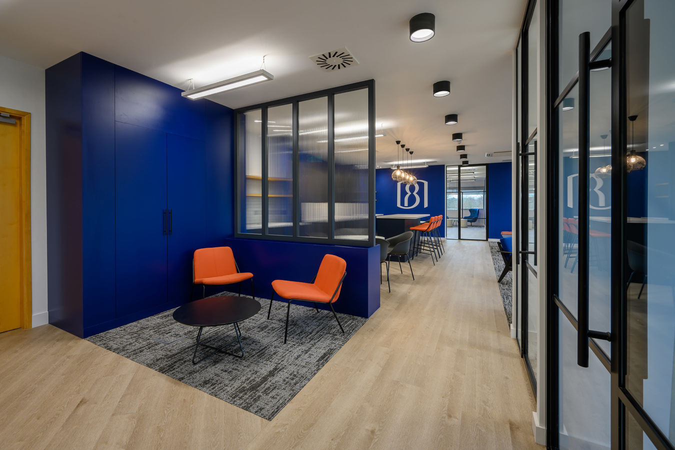 Bold office waiting area with orange seating, blue feature wall, and glass partitions, delivered by COEL for BioMed Realty.