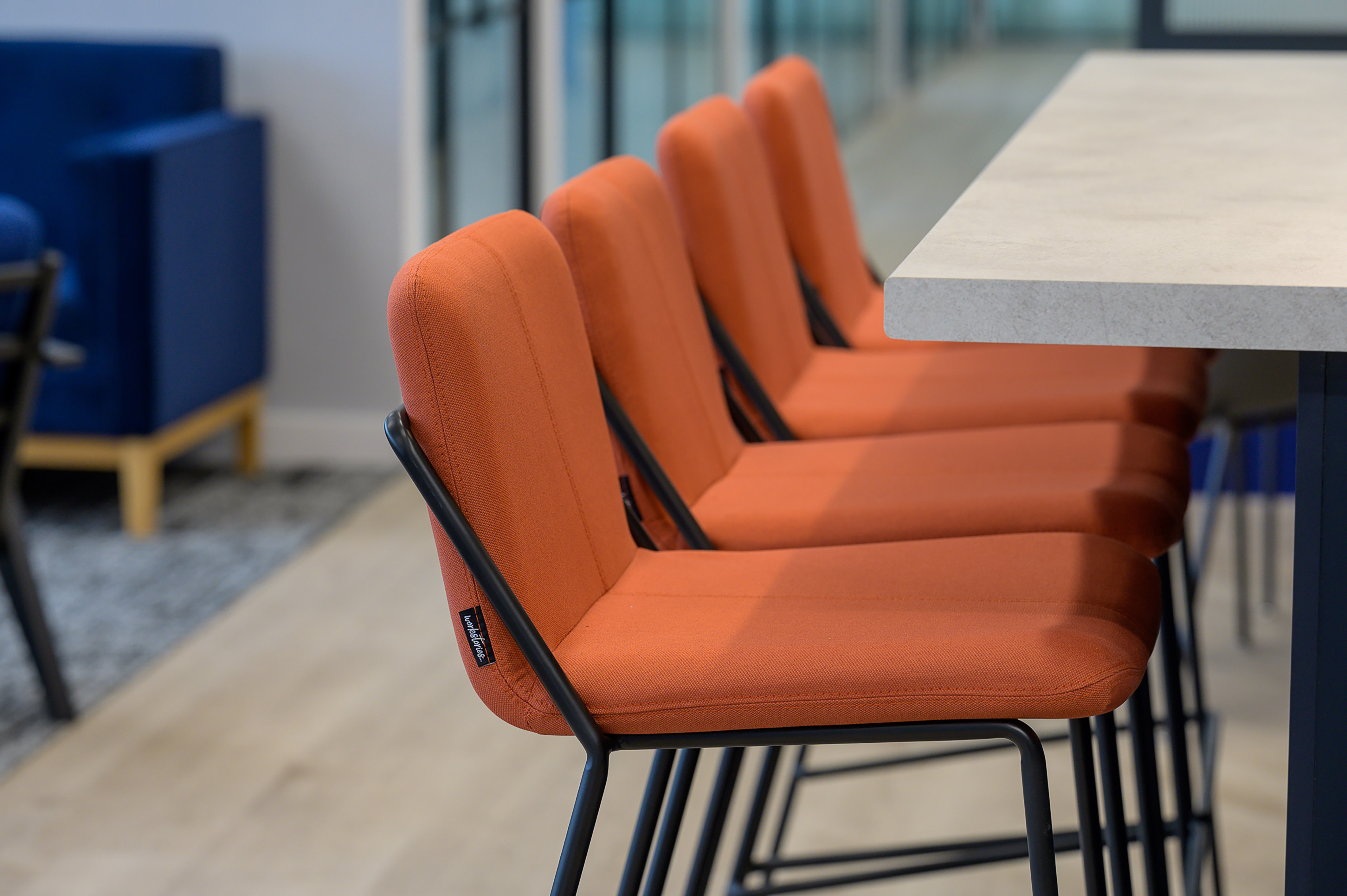 Orange upholstered chairs are lined up at a light-colored tabletop in a modern office setting.