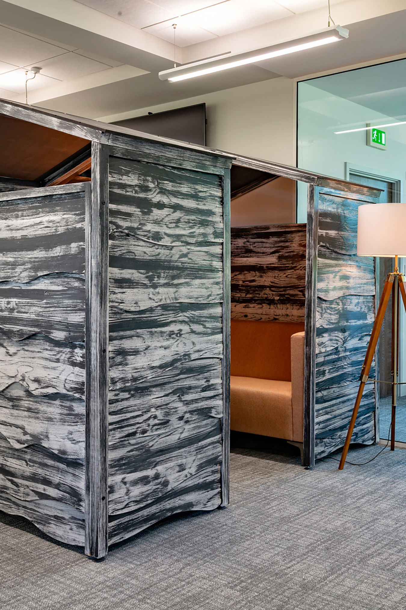 Stylish office space with rustic wooden meeting pods, floor lamp, and coat stand. Large windows bring natural light, creating a modern, inviting atmosphere