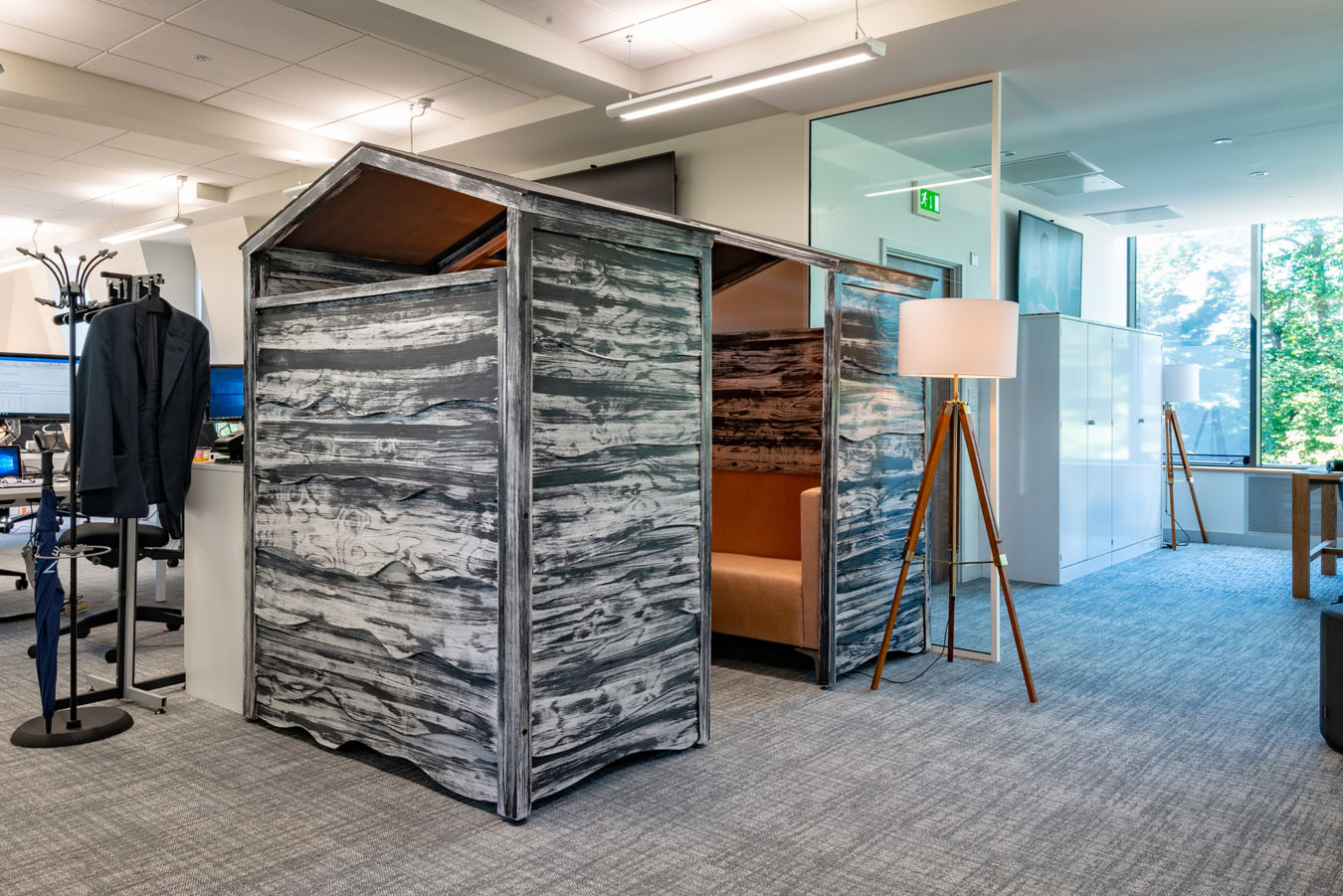 Stylish office space with rustic wooden meeting pods, floor lamp, and coat stand. Large windows bring natural light, creating a modern, inviting atmosphere
