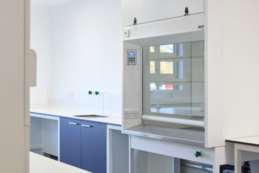 Modern laboratory with blue cabinets and a white fume hood on the right. Bright lighting and clean surfaces create a sterile, professional atmosphere
