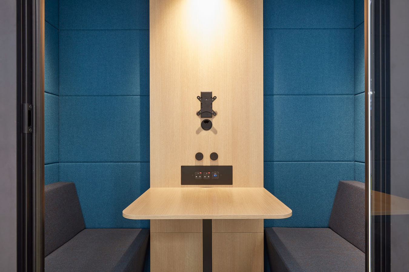 inside of a one person booth, with a wooden panel in the centre, a green stool and dark blue soft walls
